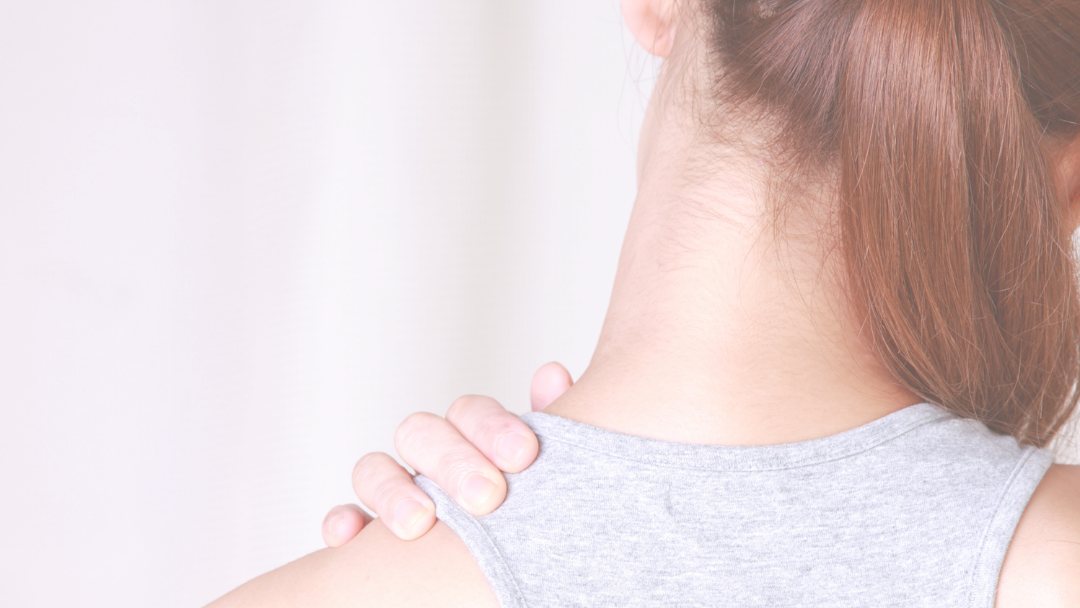 A woman holding the top of her shoulder near the neck